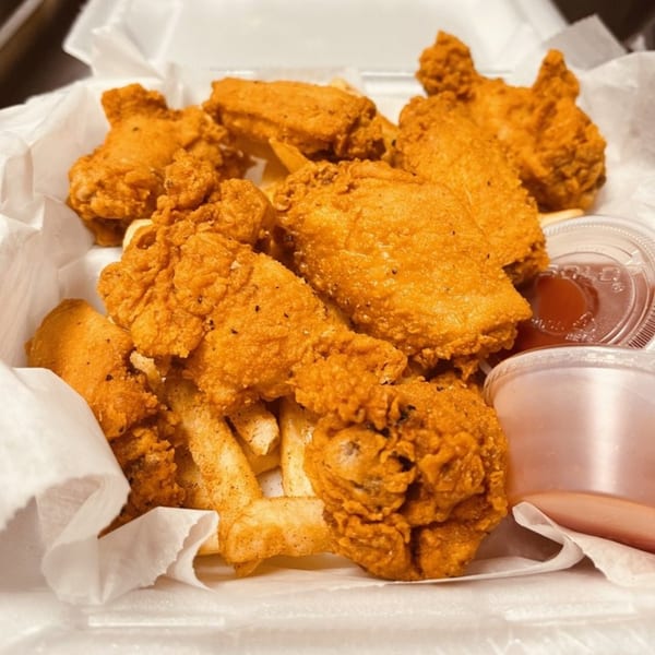 Golden fried chicken and french fries in a takeout container with dipping sauces.