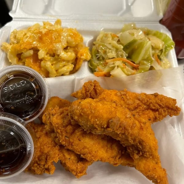 A soul-food meal with fried chicken tenders, mac and cheese, and cabbage in a takeout container.