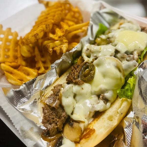 Cheesesteak with melted cheese, jalapeños, and lettuce, served with waffle fries in a foil-lined basket.