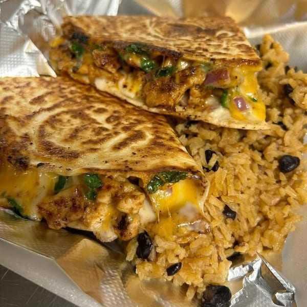 Two cheesy quesadilla halves filled with chicken and vegetables, served with rice and black beans.