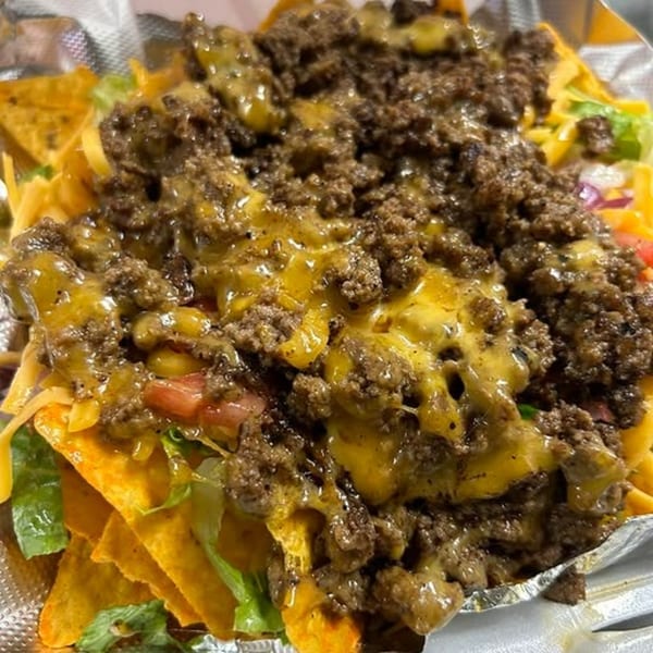 Soul food nachos with seasoned ground beef, melted cheese, lettuce, and diced tomatoes.